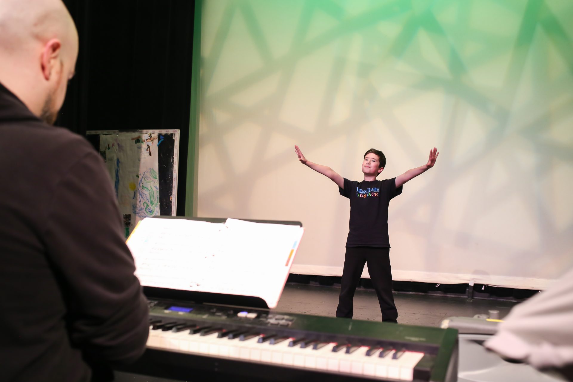 A student standing in front of a piano, arms raised.