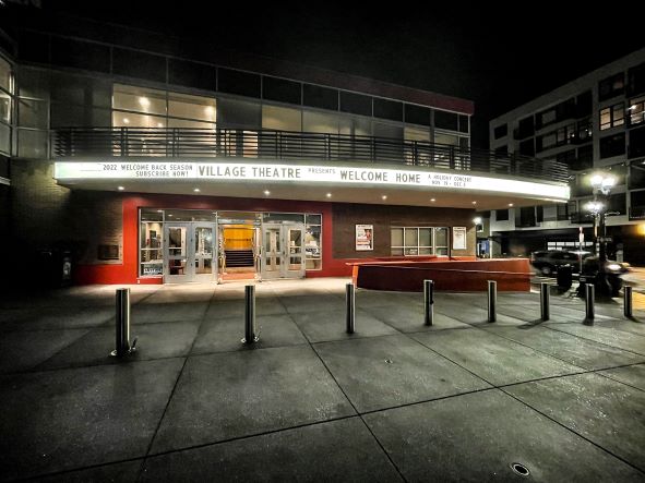Outside of a red and white building with a white glowing marquee reading "Everett Performing Arts Center" and "Welcome Home"